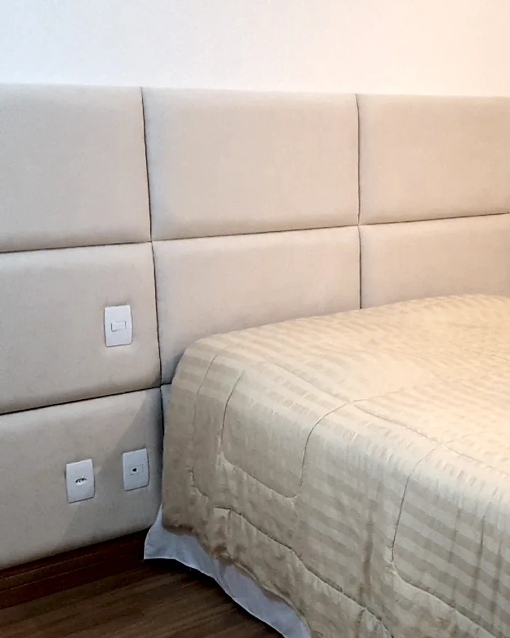 Quarto com cabeceira estofada cobrindo a parede inteira em módulos quadrados na cor bege claro.