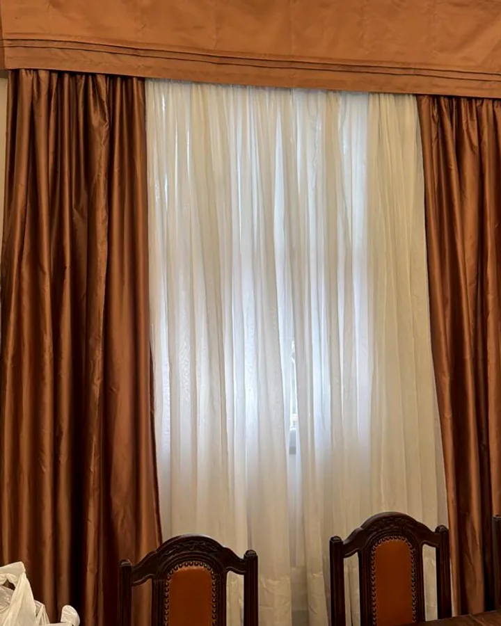 Cortina clássica com bandô e xales em tom cobre em sala de jantar com móveis de madeira escura.