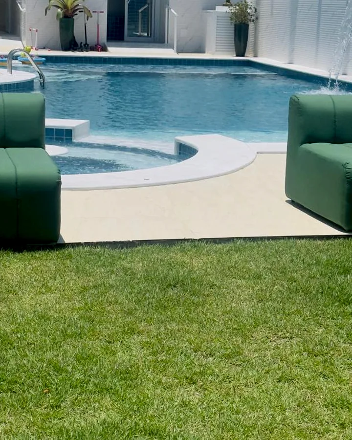 Duas poltronas modulares verdes sem braço posicionadas na borda de uma piscina em área externa ensolarada.