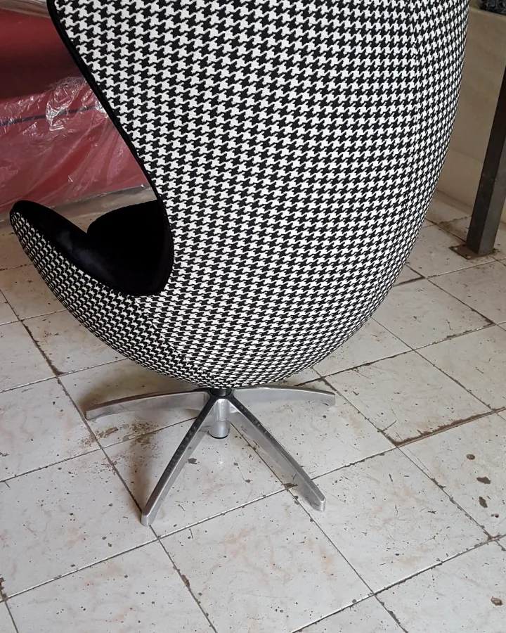 Vista traseira de poltrona modelo Egg estofada em tecido padrão pied-de-poule preto e branco com base metálica.