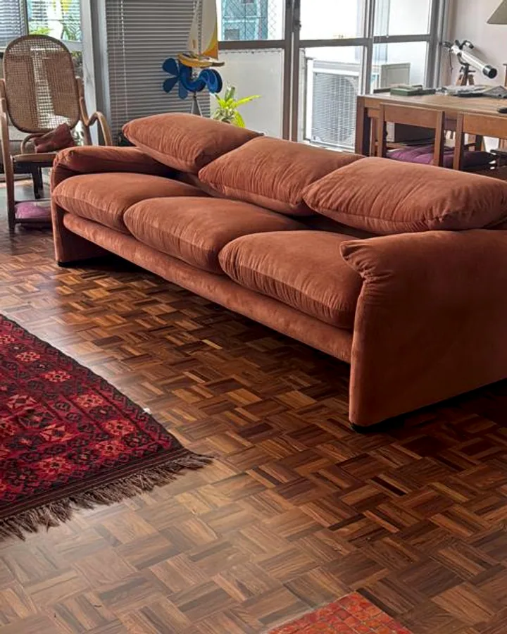 Sofá de veludo cotelê na cor terracota com design curvo e almofadas robustas, ambientado em sala com piso de madeira.